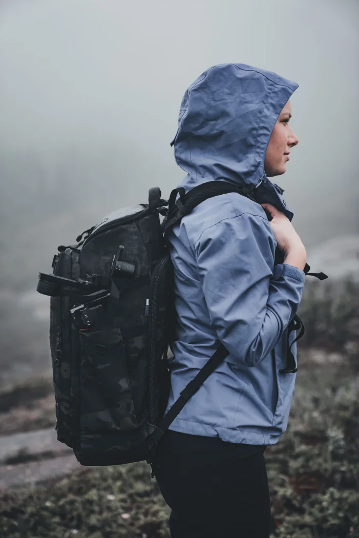 Eine Wanderin mit Kapuzenjacke und Rucksack im Nebel.