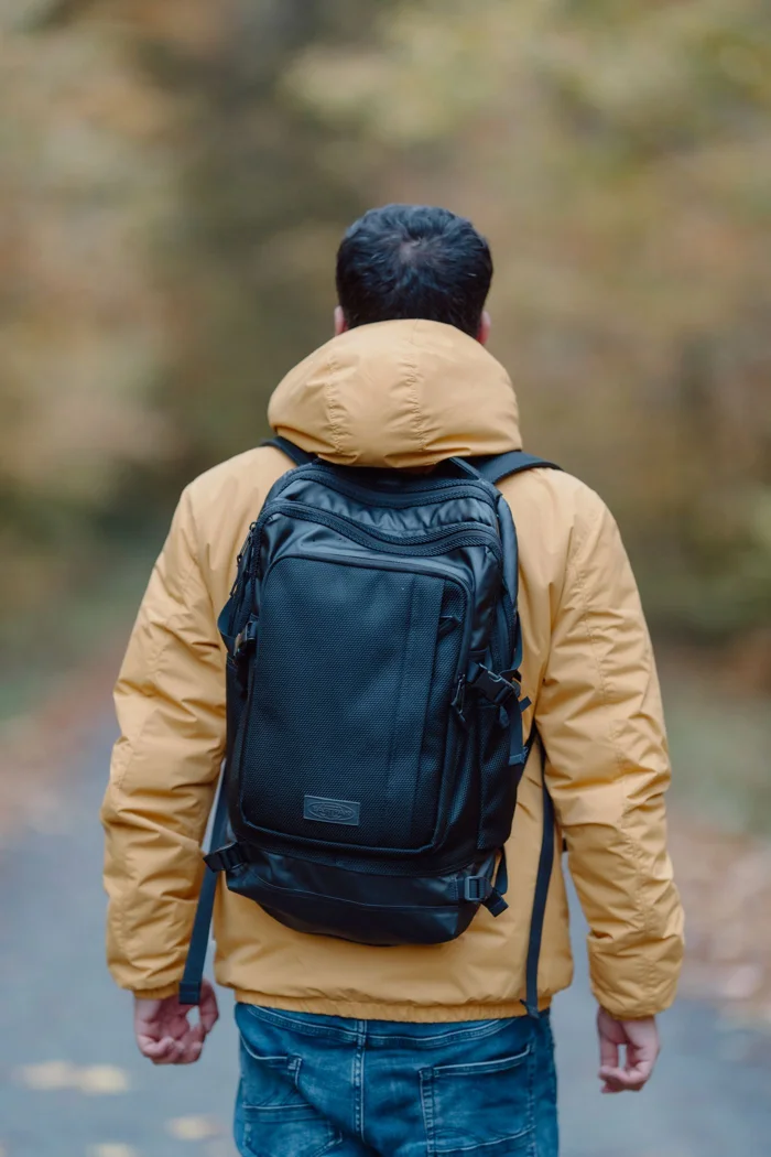 A yellow rain jacket worn beneath a backpack on a forest path.