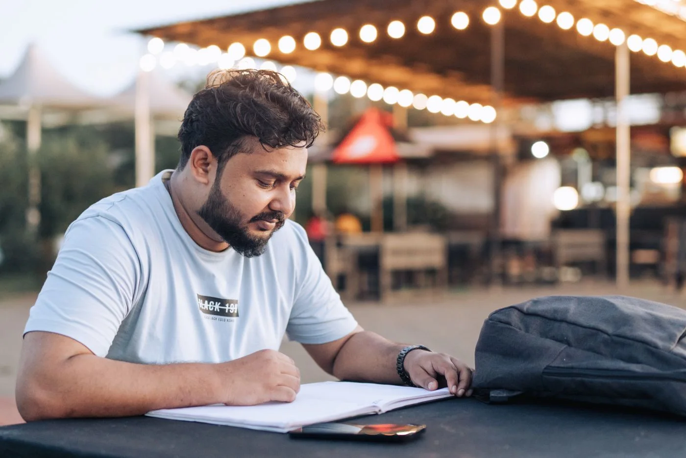 Writing notes at a table beside a backpack.